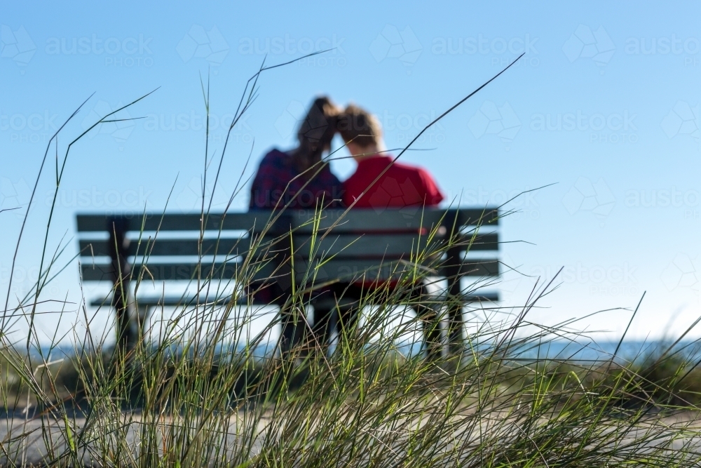 Couple from behind in private moment of park bench - Australian Stock Image