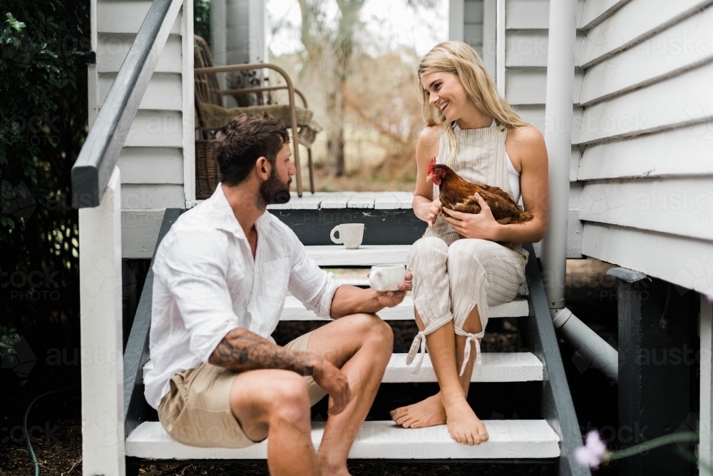 Couple having a cup of coffee on steps of verandah, with woman holding a chicken. : Austockphoto Couple having a cup of coffee on steps of verandah, with woman holding a chicken. - Australian Stock Image