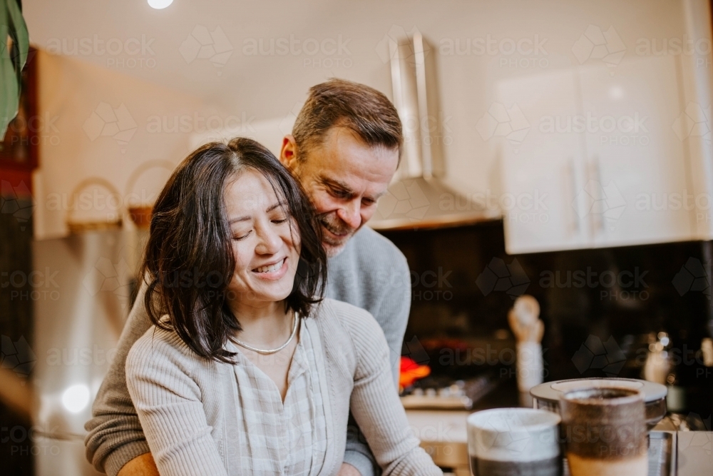 Couple hugging and working in kitchen - Australian Stock Image