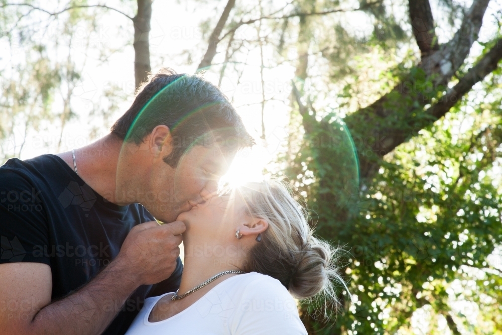 Couple kissing outside with lens flare - Australian Stock Image