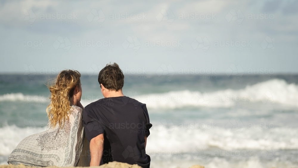 Couple on sitting on beach looking outwards - Australian Stock Image