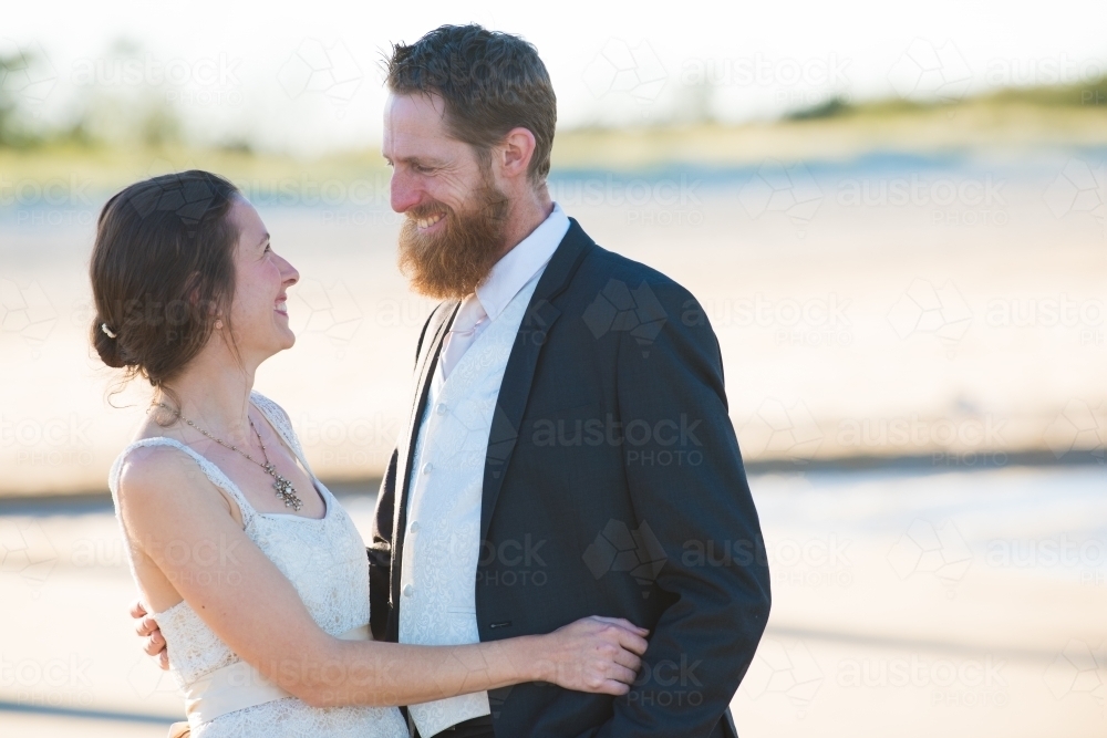 Couple on wedding day looking at each other smiling against an outdoor backdrop. - Australian Stock Image