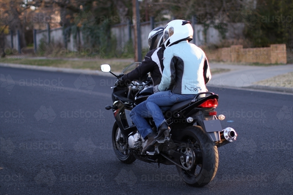 Couple riding a motorbike on a suburban street - Australian Stock Image