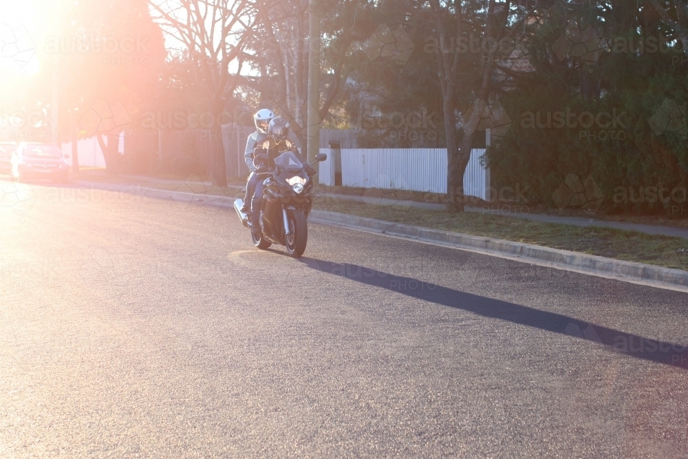 Couple riding motorbike on suburban street - Australian Stock Image
