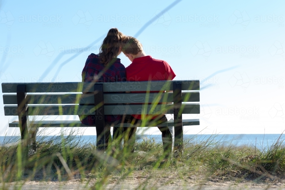Couple seen from behind close together on park bench - Australian Stock Image