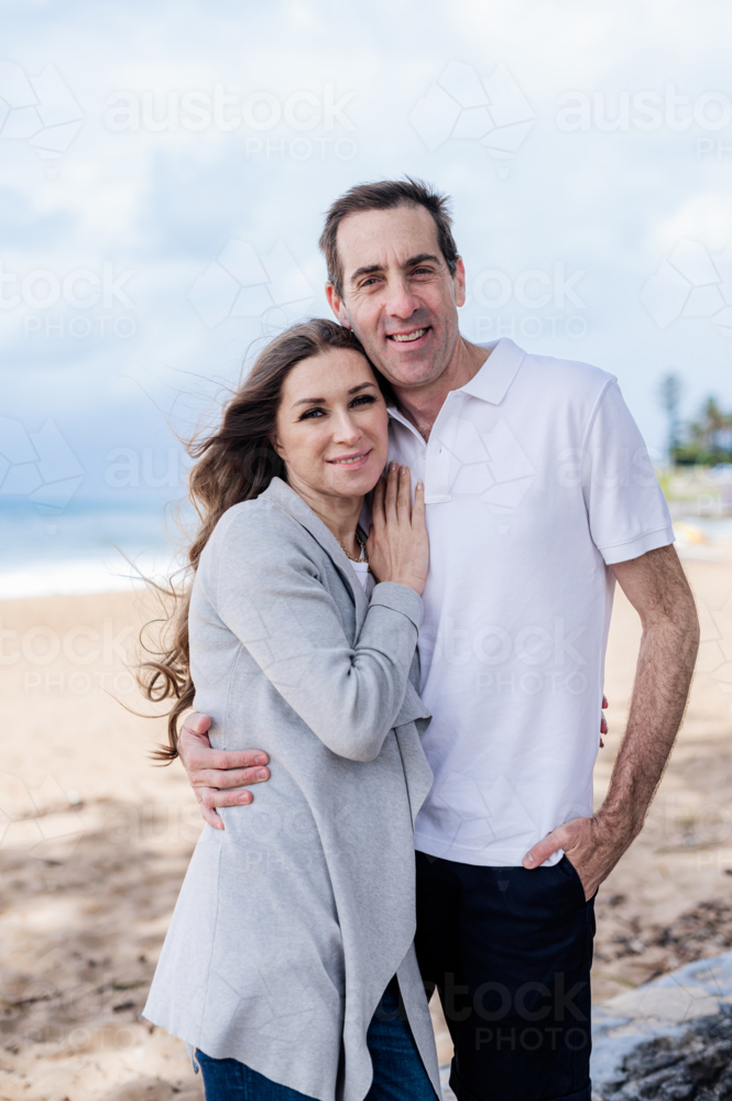 Couple standing closely together on sandy beach with ocean in the background - Australian Stock Image