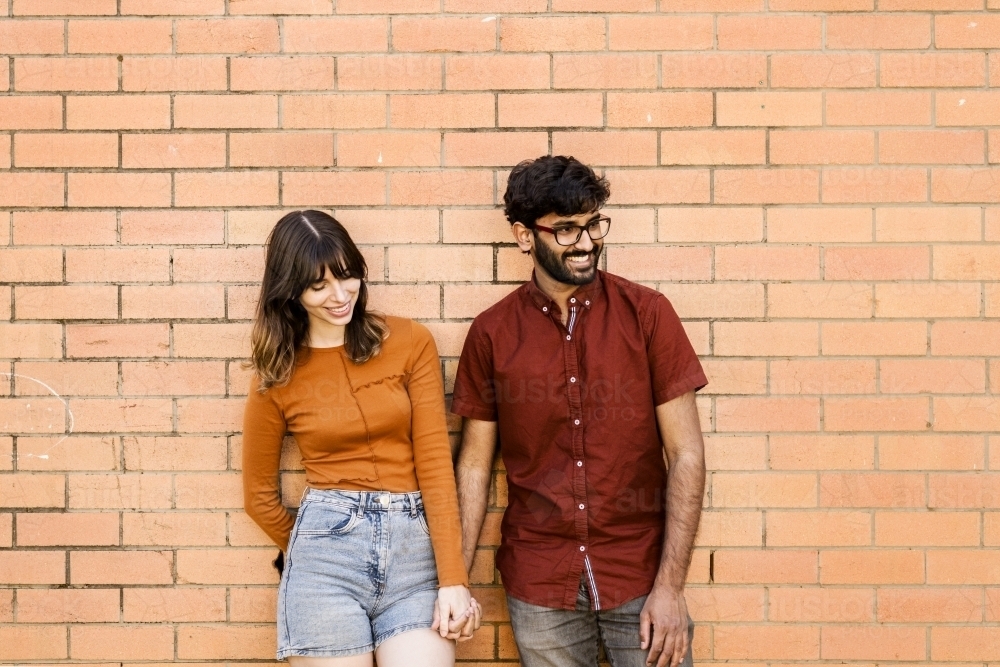 couple standing together leaning against brick wall - Australian Stock Image