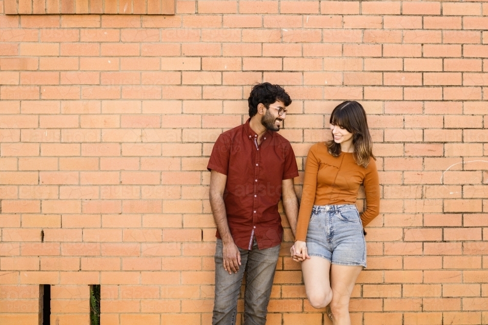 couple standing together leaning against brick wall - Australian Stock Image