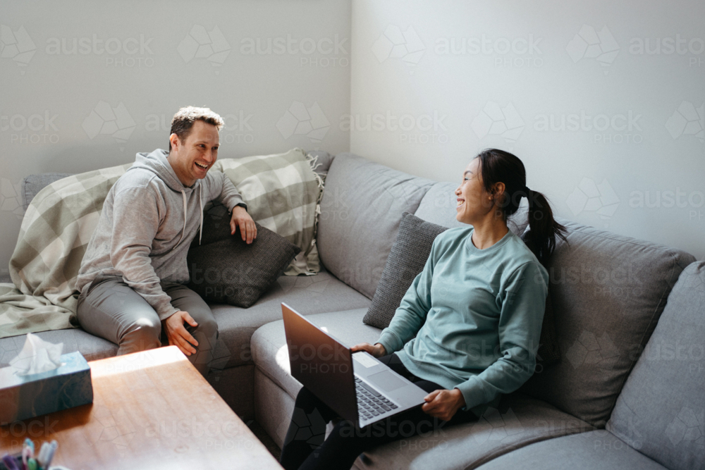 Couple talking while seated on the couch while woman holds a laptop - Australian Stock Image