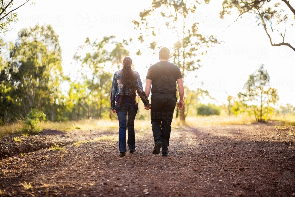 Couple walk up hill hand in hand along track - Australian Stock Image