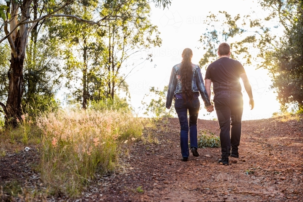Couple walk up hill hand in hand along track - Australian Stock Image