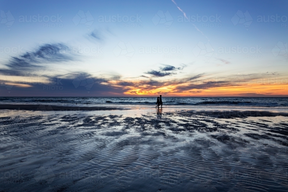 couple walking along beach at sunset - Australian Stock Image