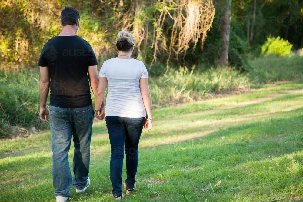Couple walking away through park holding hands - Australian Stock Image
