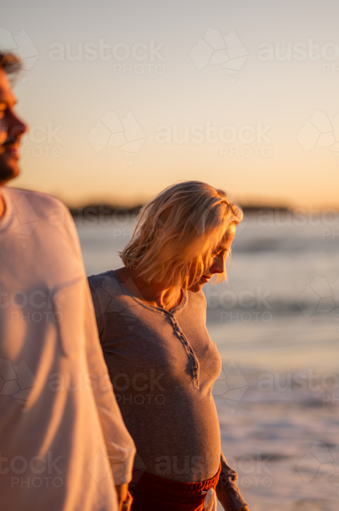 Couple walking hand in hand at Manly Beach during sunrise, celebrating maternity and family - Australian Stock Image