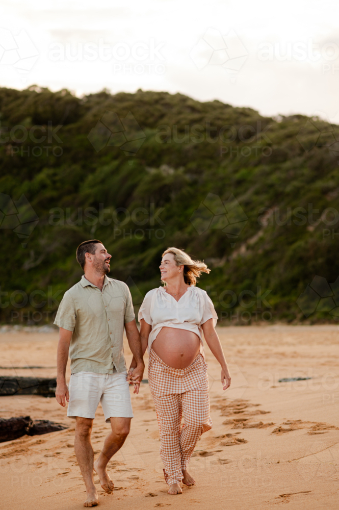 Couple walking hand in hand on the beach during sunset with pregnancy glow - Australian Stock Image