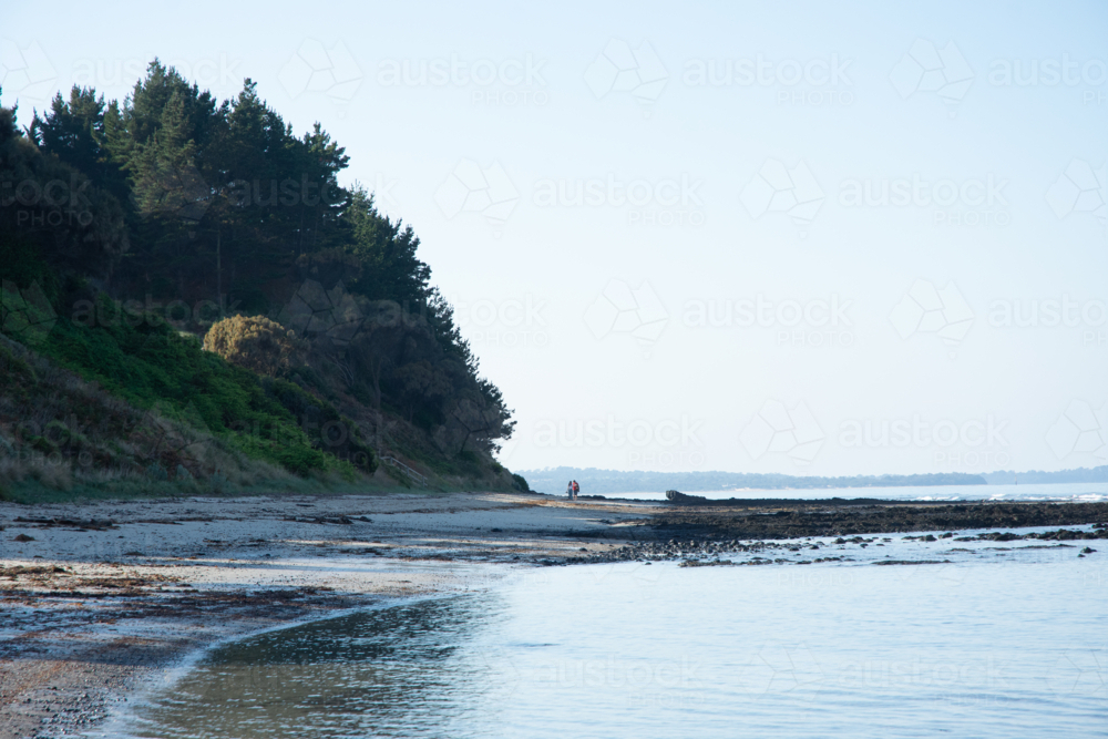 Couple walking on beach at late afternoon on calm day - Australian Stock Image