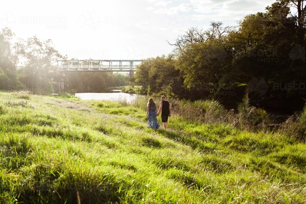 Couple walking on grass at riverside in country - Australian Stock Image