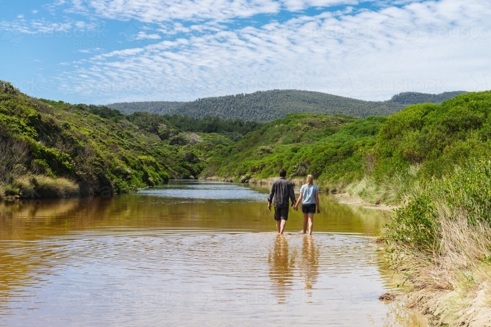 couple walking up a creek by the beach - Australian Stock Image