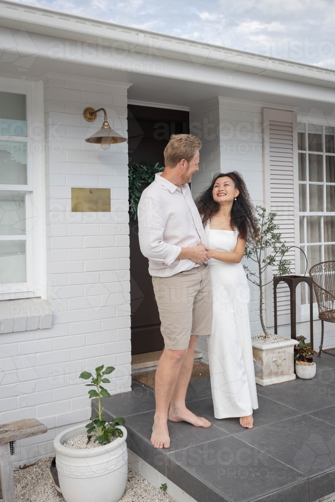 Couple wearing white standing together on front porch - Australian Stock Image