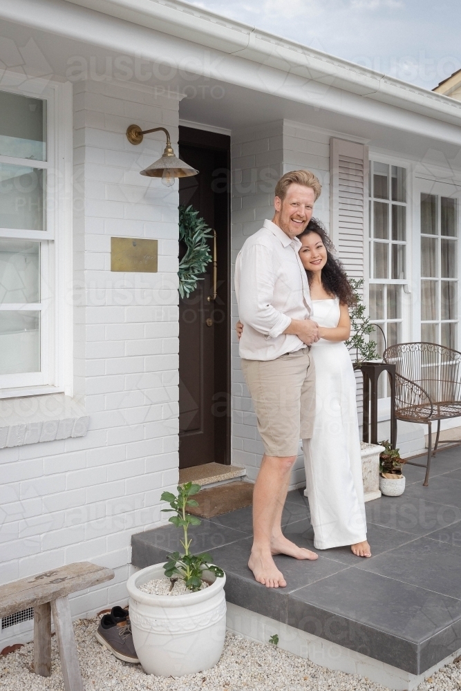 Couple wearing white standing together on front porch - Australian Stock Image