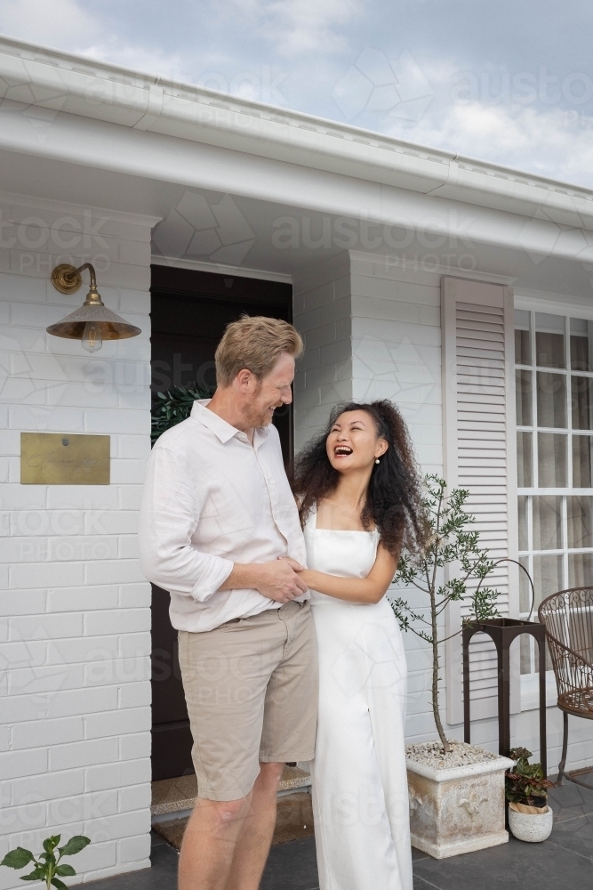 Couple wearing white standing together on front porch - Australian Stock Image