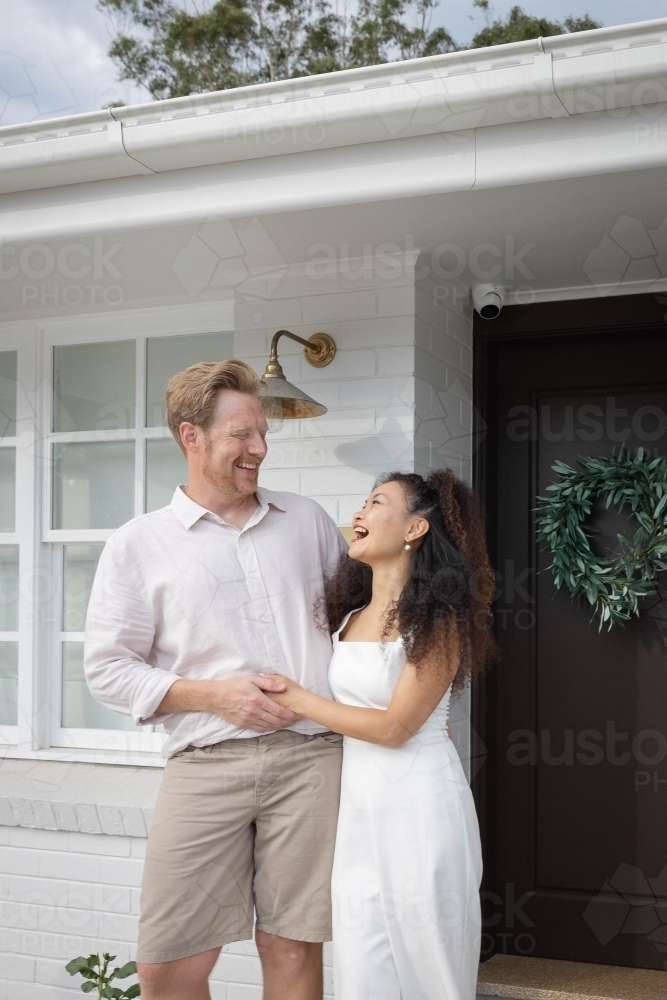 Couple wearing white standing together on front porch - Australian Stock Image