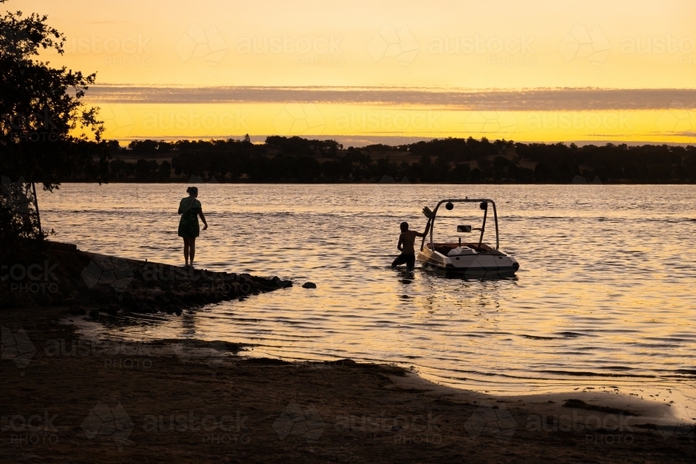 couple with speedboat at boat ramp on lake at sunset - Australian Stock Image
