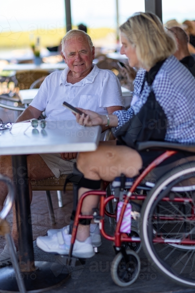 couple with woman in wheelchair sitting at cafe table - Australian Stock Image