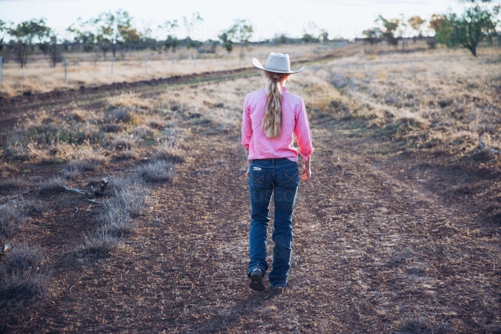 Cowgirl walking away on dirt road - Australian Stock Image