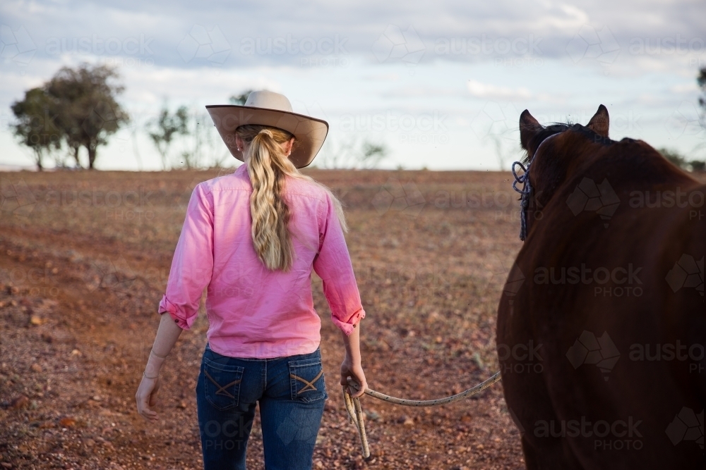 Cowgirl walking horse along dirt road - Australian Stock Image