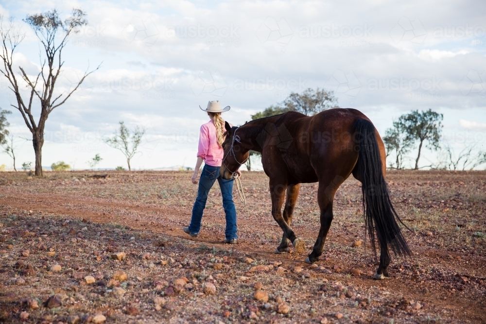 Cowgirl walking horse on rocky outback road - Australian Stock Image