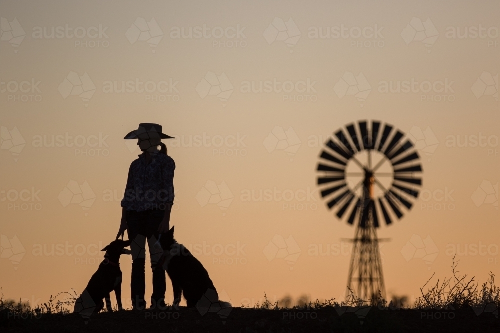 Cowgirl with dogs and windmill silhouette - Australian Stock Image