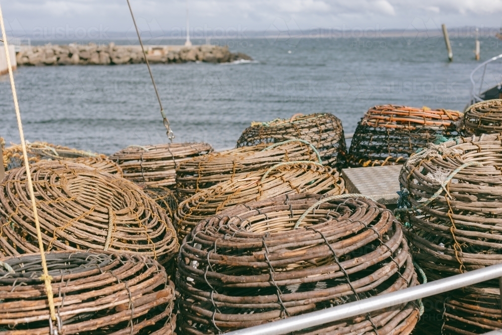 Crayfish pots on a commercial fishing boat at a wharf beside ocean - Australian Stock Image