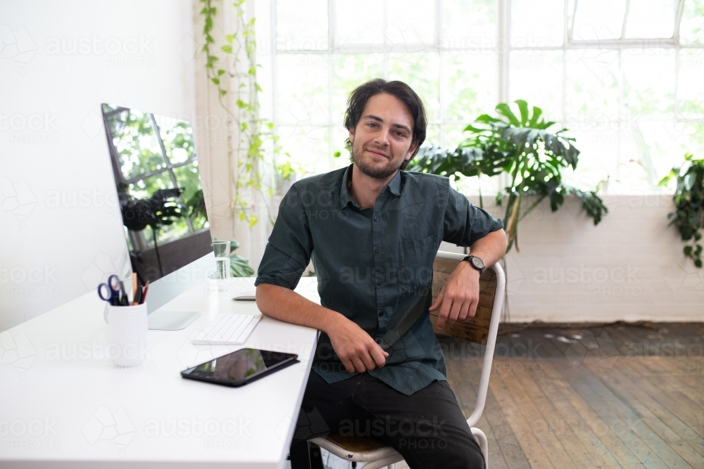 Creative businessman sitting in front of his desk in studio environment - Australian Stock Image