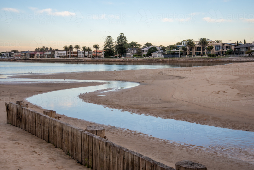 Creek flowing out to the bay past a wooden fence - Australian Stock Image