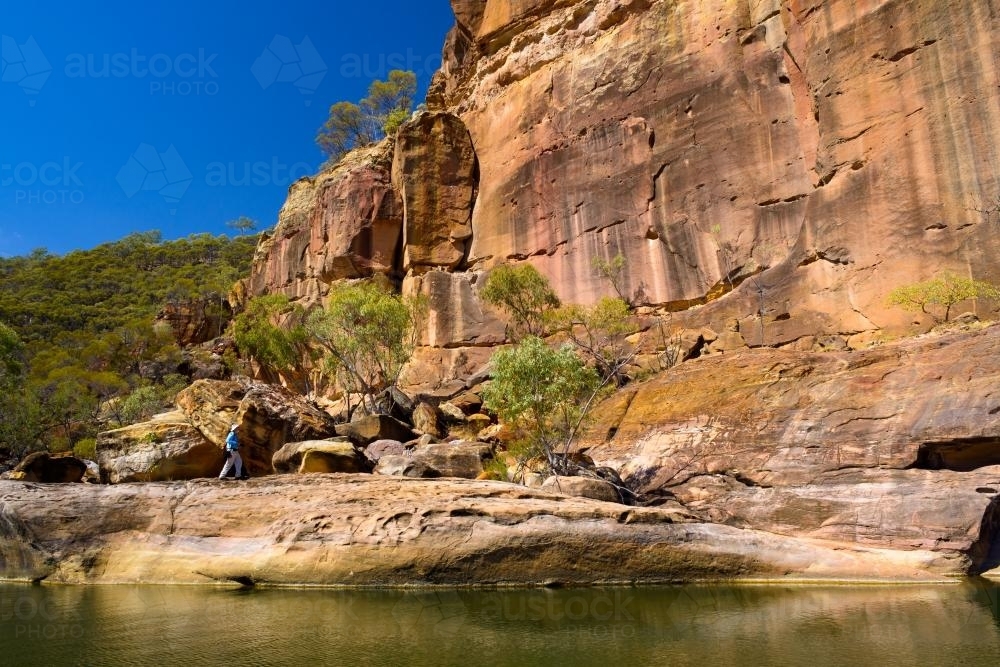 Creek in a gorge with orange sandstone rock formation and blue sky - Australian Stock Image