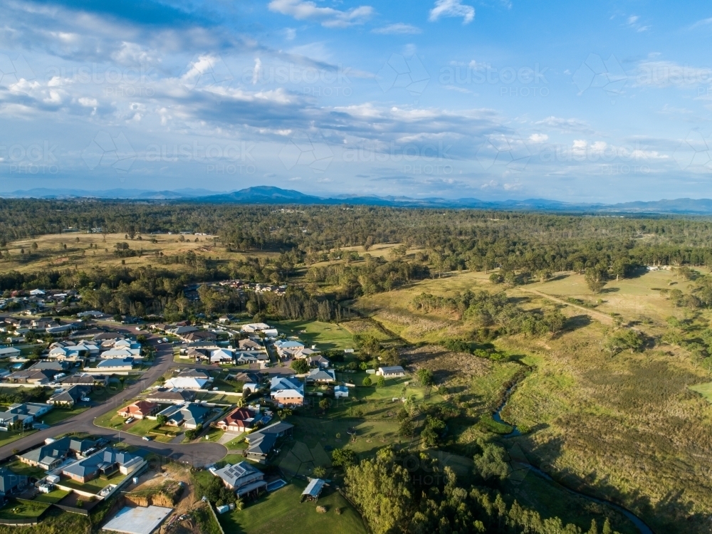Creek winding through farmland behind houses at edge of residential area - Australian Stock Image