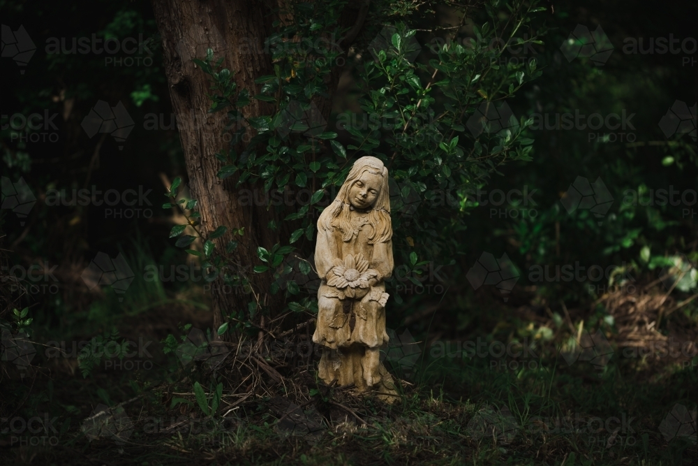 Creepy girl statue with broken neck in moody forest setting - Australian Stock Image