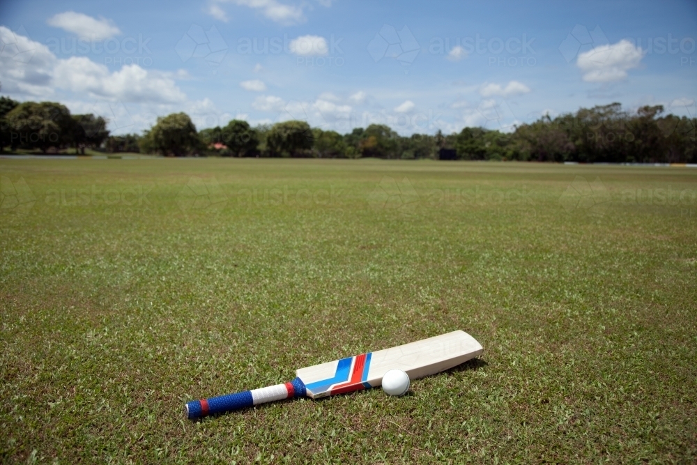 Cricket bat and ball lying on grass field - Australian Stock Image