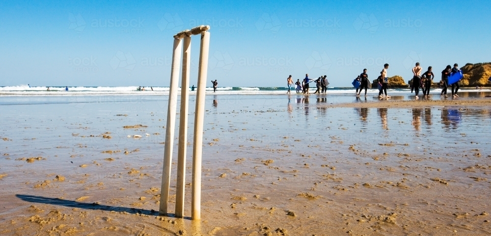 Cricket stumps on a beach with surfers in background - Australian Stock Image