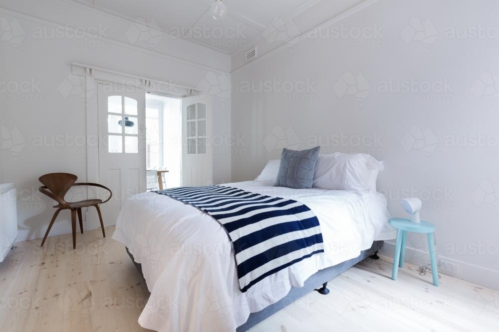 Crisp white Danish stylish bedroom with striped throw rug and blue side table - Australian Stock Image
