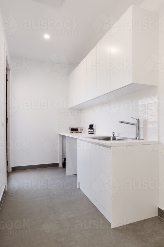 Crisp white laundry with overhead cupboards and chrome tapware - Australian Stock Image