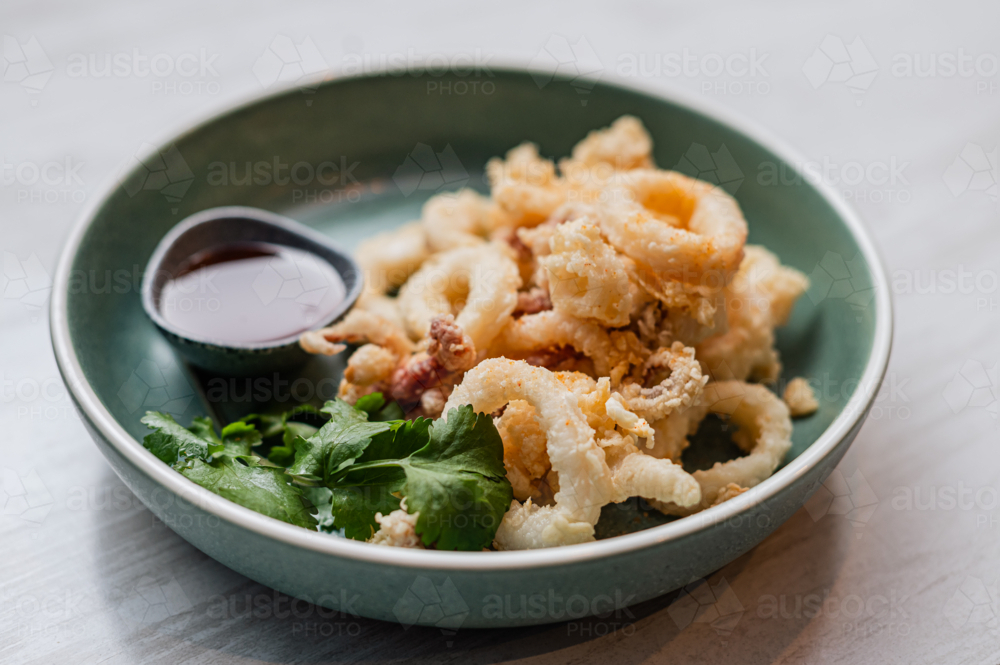 Crispy fried calamari rings in a bowl, with by a side sauce of coriander - Australian Stock Image