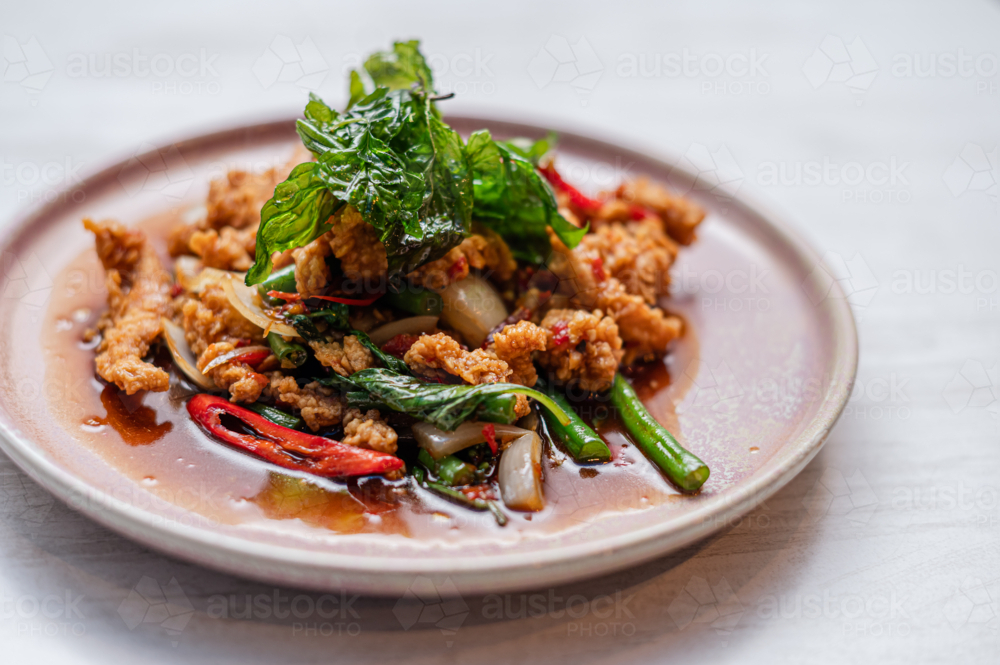 Crispy fried chicken tossed with fresh herbs and colourful vegetables - Australian Stock Image