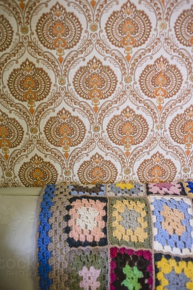 Crochet blanket draped over couch with wallpapered wall - Australian Stock Image