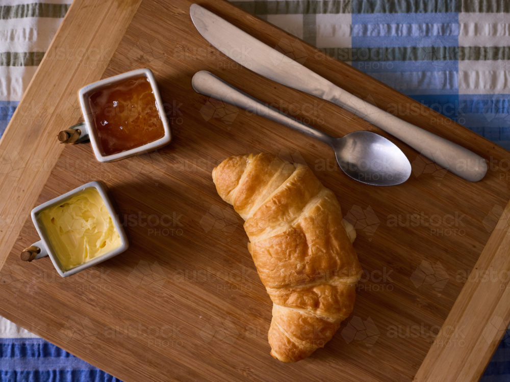 Croissant, butter & jam on bread board, top down view. - Australian Stock Image