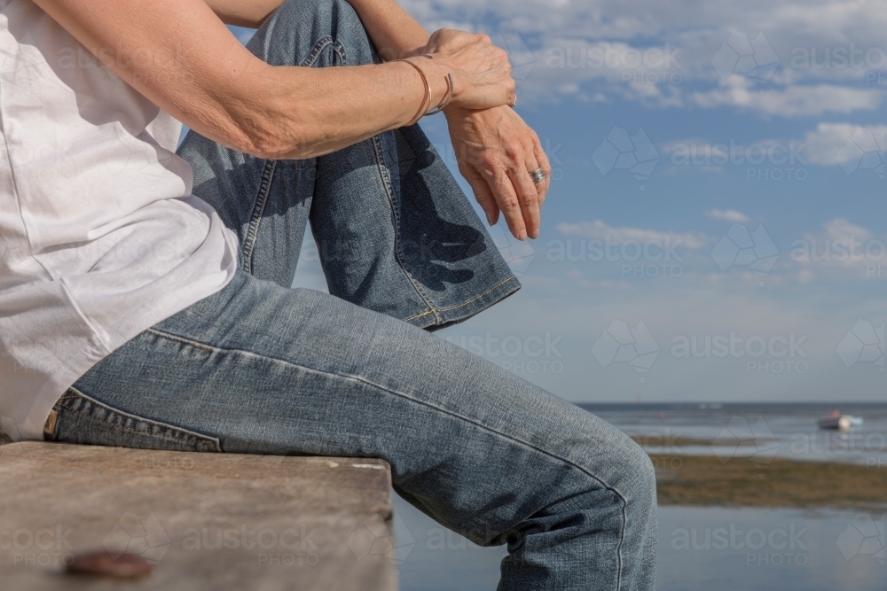 Cropped body shot of woman relaxing on timber jetty - Australian Stock Image