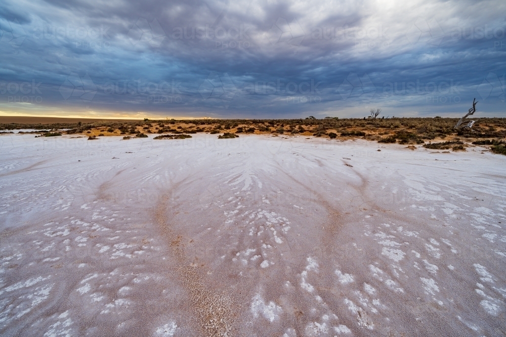 Crusty salt patterns on a dry lake bed under a gloomy sky - Australian Stock Image