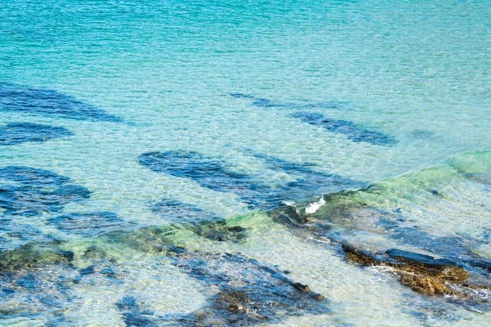 Crystal clear, blue sea water rippling over rocks and white sand - Australian Stock Image