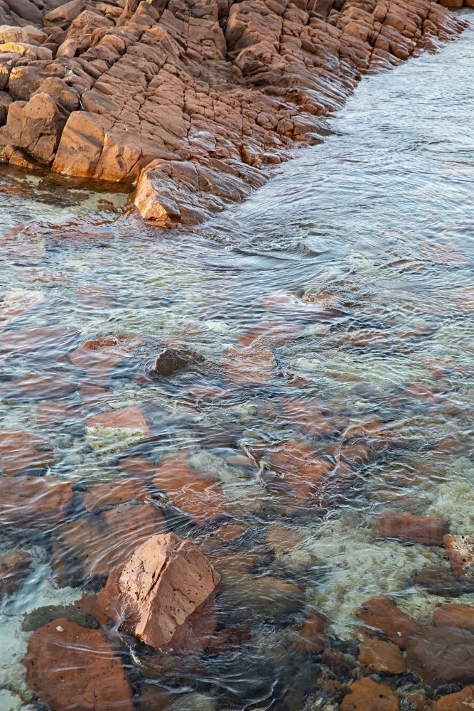 Crystal clear water flowing over a bed of reddish-brown rocks - Australian Stock Image